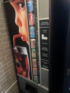 A soda vending machine used by a small vendor, featuring a mix of Pepsi and Coca-Cola products with a retro-style advertisement of a child drinking from a straw.